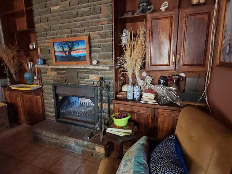 Living room featuring a prominent brick fireplace, extensive built-in wooden cabinetry, and traditional tiled flooring with a timber-clad ceiling.