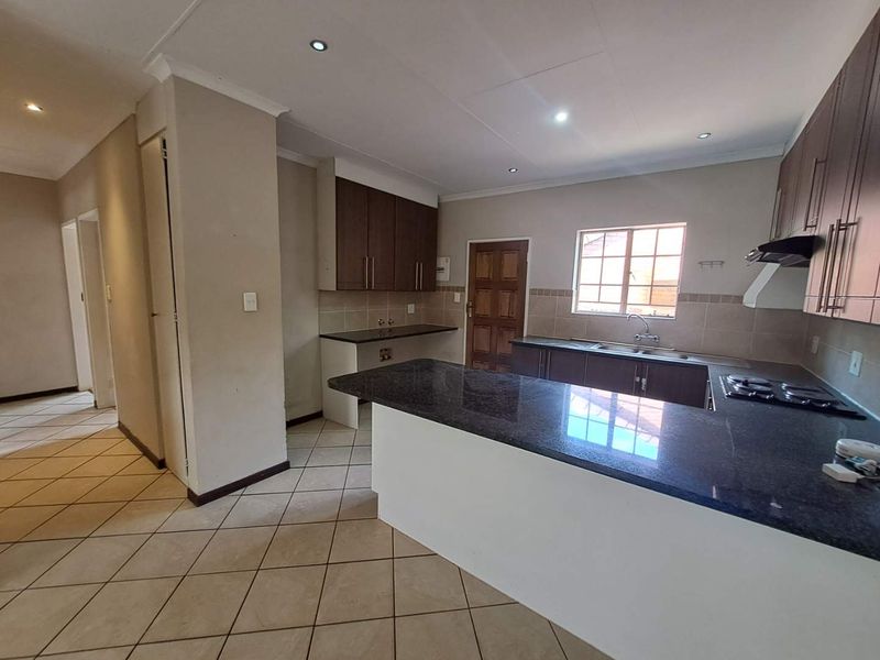 Spacious kitchen featuring dark wood cabinetry, granite countertops, a gas hob with extractor, and tiled flooring, offering a functional layout for cooking and preparation.