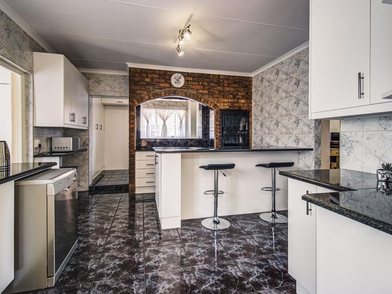 A functional kitchen featuring granite countertops, white cabinetry, an exposed brick feature wall, and a breakfast bar with tiled flooring.
