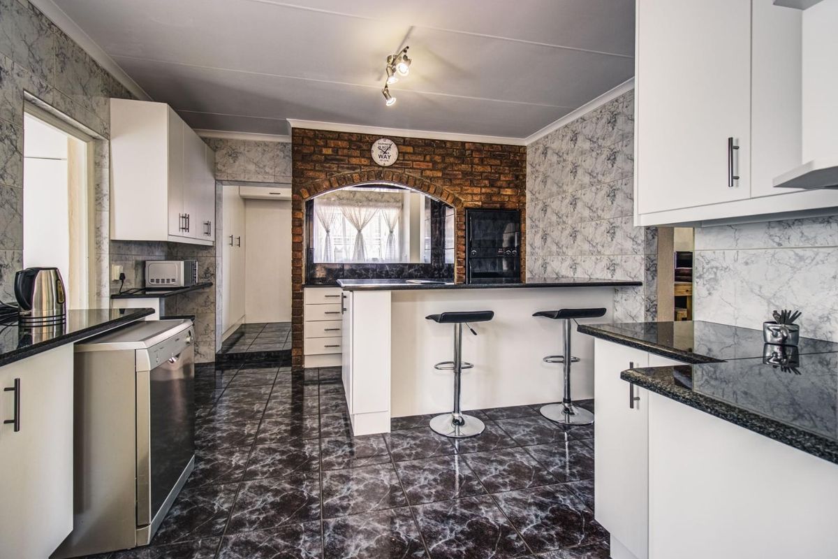 A functional kitchen featuring granite countertops, white cabinetry, an exposed brick feature wall, and a breakfast bar with tiled flooring.