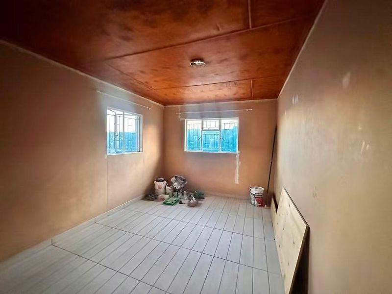 An empty bedroom featuring tiled flooring and a timber ceiling, currently undergoing minor renovations with unfinished wall surfaces.