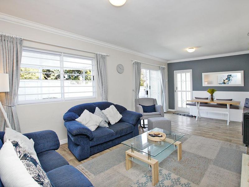 A bright and spacious living room featuring laminate flooring, crown molding, and a built-in bench seating area with access to the outdoor space.
