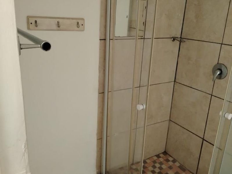 A functional bathroom shower area featuring a glass enclosure, tiled walls, and mosaic floor tiling, currently requiring minor maintenance and cosmetic updates.