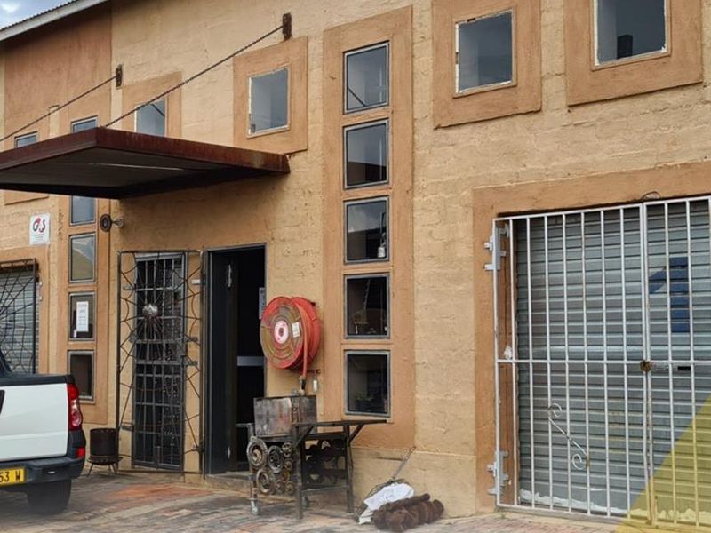 Exterior view of a mixed-use building featuring textured facade, metal security gates, fire hose reel, and a prominent metal awning over the entrance.