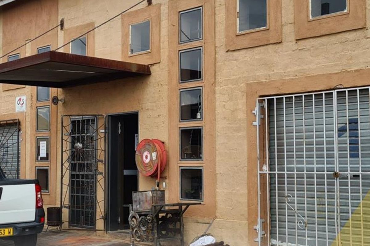 Exterior view of a mixed-use building featuring textured facade, metal security gates, fire hose reel, and a prominent metal awning over the entrance.