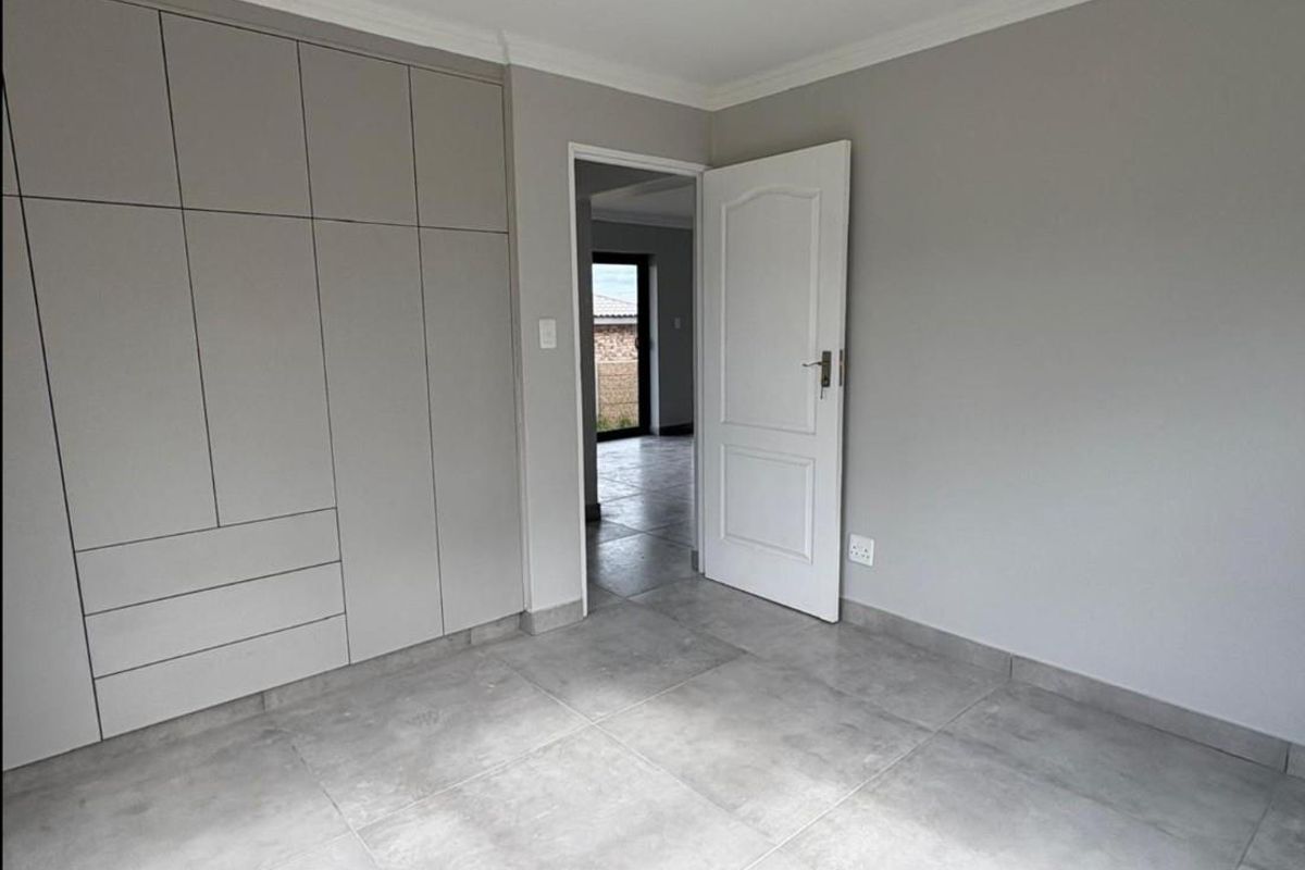 A clean, modern bedroom featuring neutral grey floor tiles, built-in cabinetry, and a doorway leading to an adjacent living space.
