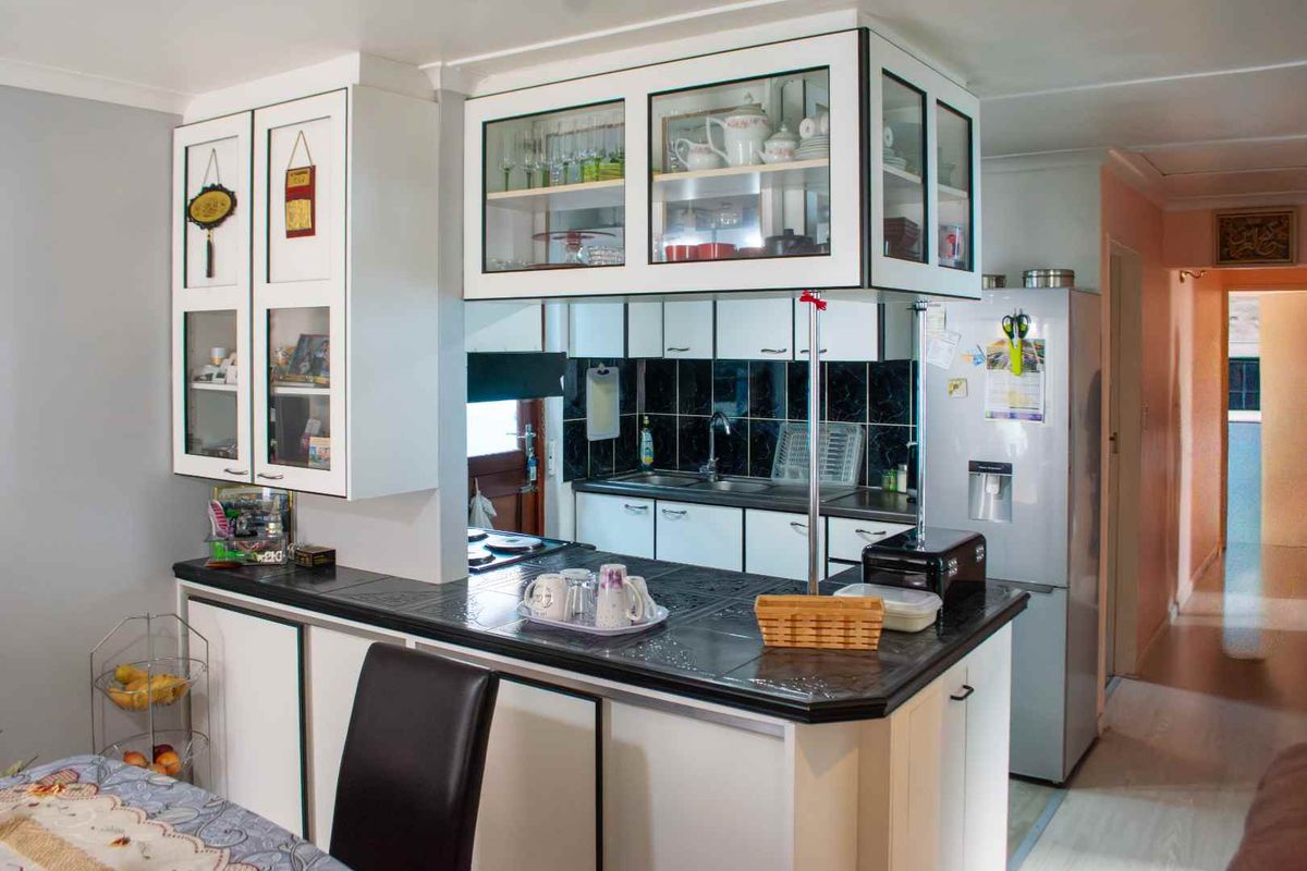 A functional kitchen featuring white cabinetry with glass-fronted upper units, dark tiled countertops, and a tiled backsplash, providing a practical workspace.