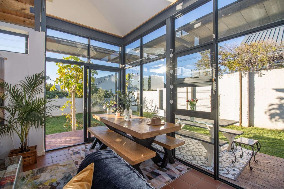 A bright, modern sunroom featuring floor-to-ceiling glass walls, exposed rafters, and direct access to the rear garden.