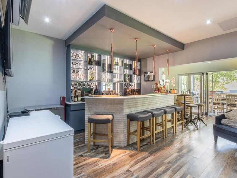 A well-appointed indoor bar area featuring a built-in counter, custom shelving, pendant lighting, and direct access to an outdoor patio through sliding glass doors.