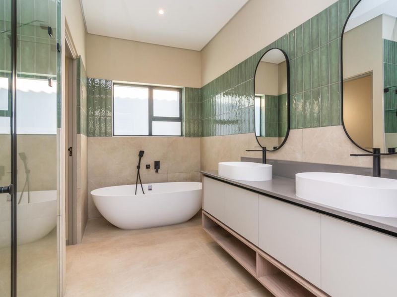Modern bathroom featuring a freestanding bathtub, double vanity with vessel sinks, and stylish green tiled accents.