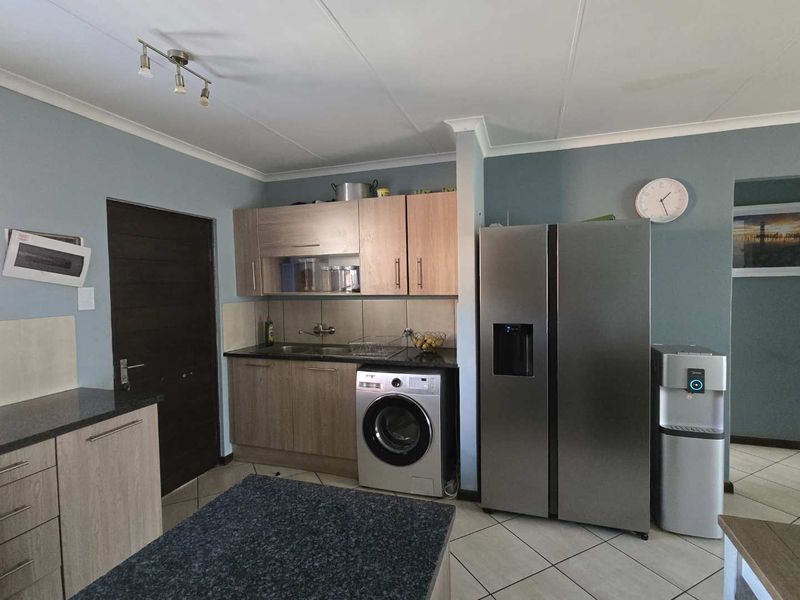 A functional kitchen featuring light wood-tone cabinetry, dark granite-look countertops, tiled flooring, and a tiled backsplash with integrated laundry and refrigeration space.