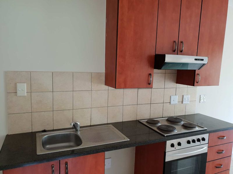 A functional kitchen featuring cherry-wood cabinetry, granite countertops, a built-in oven with electric hob, and a tiled backsplash.