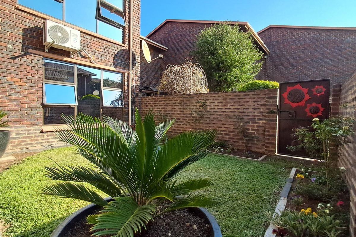 A private rear garden featuring a manicured lawn, brick boundary walls, and a secure metal gate, adjacent to the townhouse exterior.