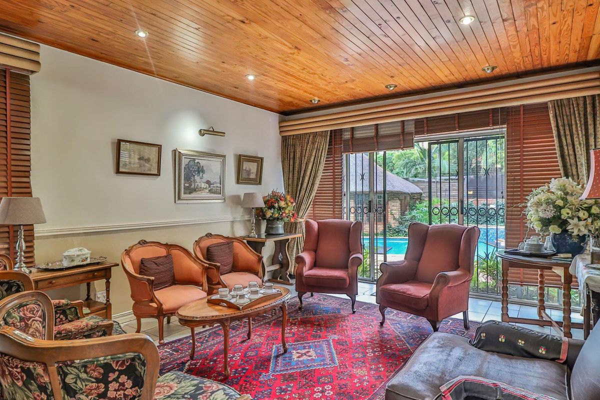 A traditional living room featuring a warm timber-paneled ceiling, tiled flooring, and sliding glass doors providing direct access to the outdoor pool area.