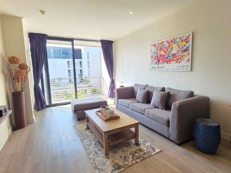A bright living room featuring laminate flooring, recessed lighting, and a large sliding glass door providing access to a private balcony.