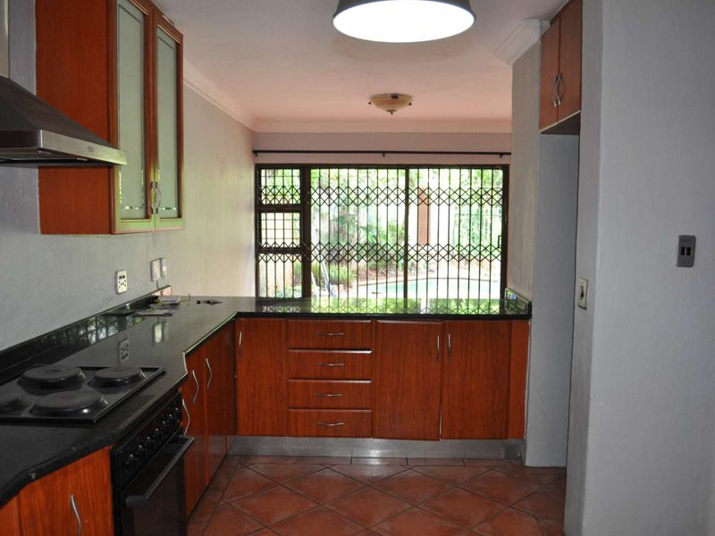 A functional kitchen featuring wood-finish cabinetry, granite countertops, and an integrated electric stove, with direct access to the outdoor area through a security gate.