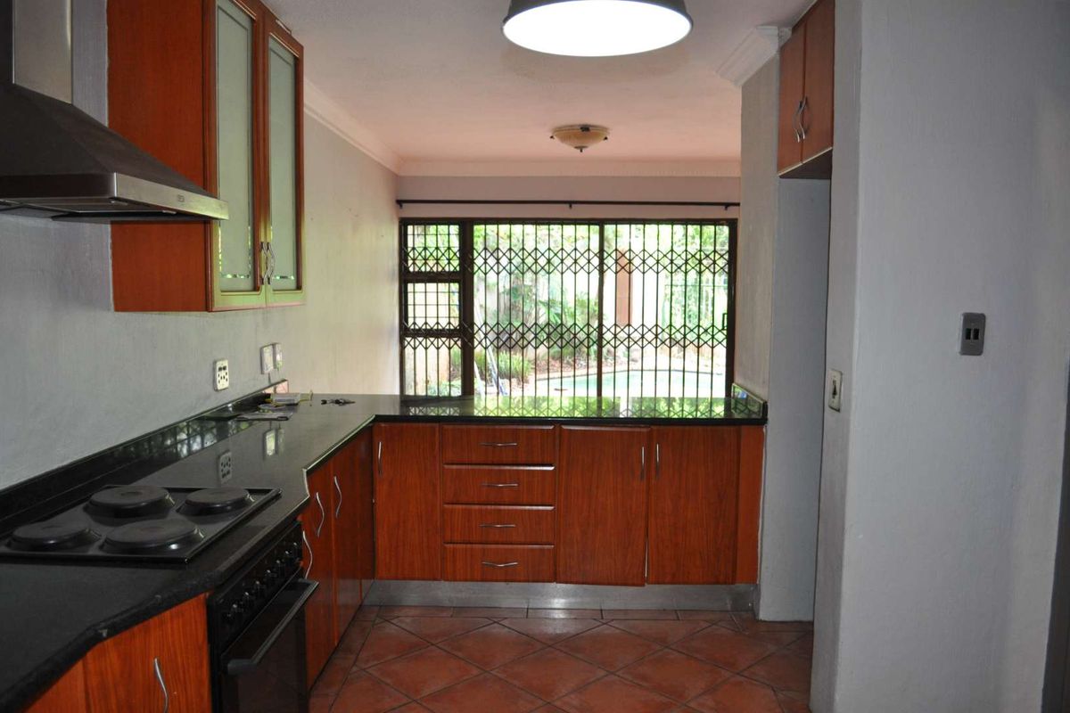 A functional kitchen featuring wood-finish cabinetry, granite countertops, and an integrated electric stove, with direct access to the outdoor area through a security gate.