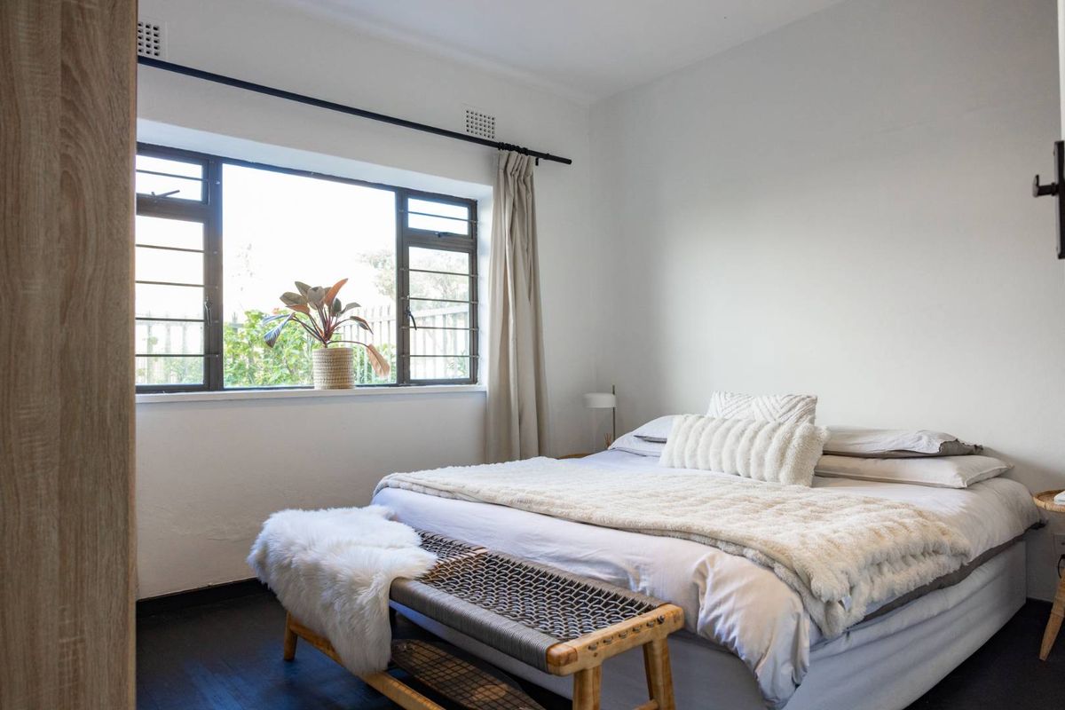 A bright and cozy bedroom featuring dark timber flooring and a large metal-framed window that allows for ample natural light.