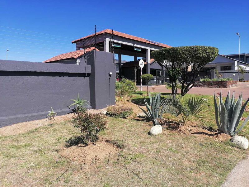 View of the secure residential estate entrance featuring a gated access point, perimeter wall with electric fencing, and maintained garden area.