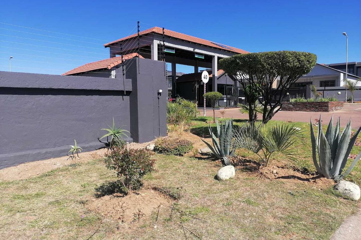 View of the secure residential estate entrance featuring a gated access point, perimeter wall with electric fencing, and maintained garden area.