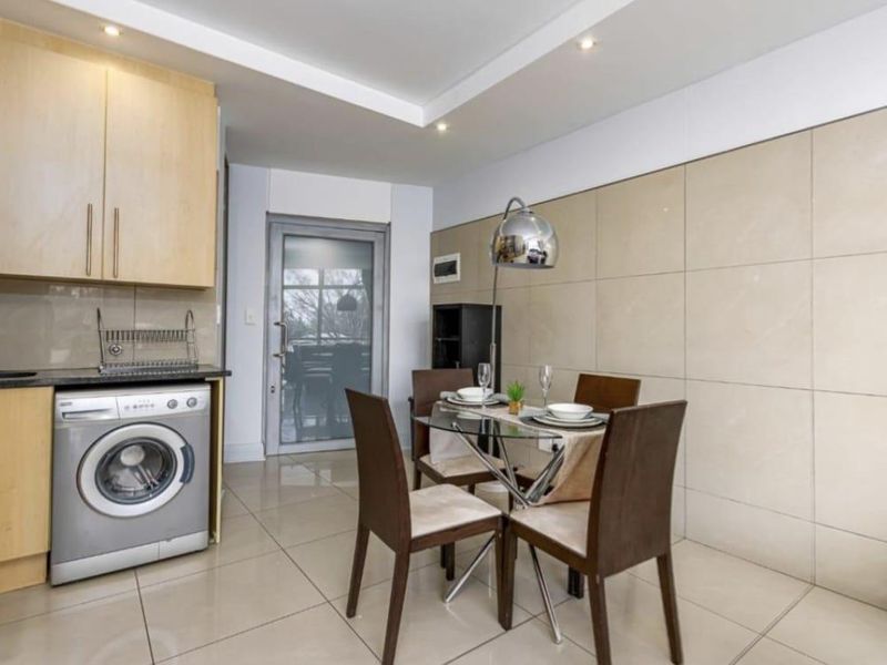 Open-plan kitchen and dining area featuring modern tiled flooring, a tiled feature wall, built-in cabinetry, and recessed ceiling lighting.