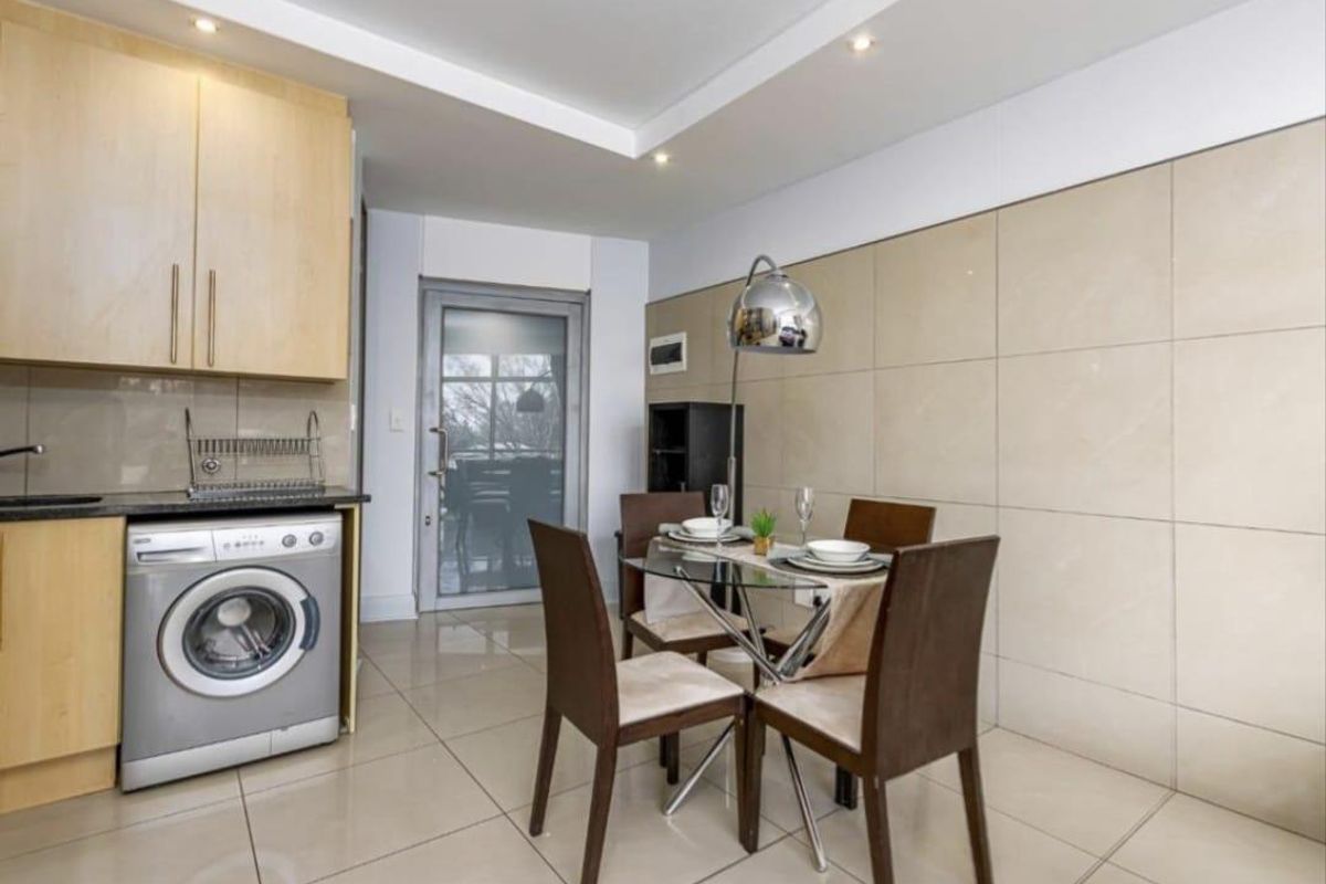 Open-plan kitchen and dining area featuring modern tiled flooring, a tiled feature wall, built-in cabinetry, and recessed ceiling lighting.