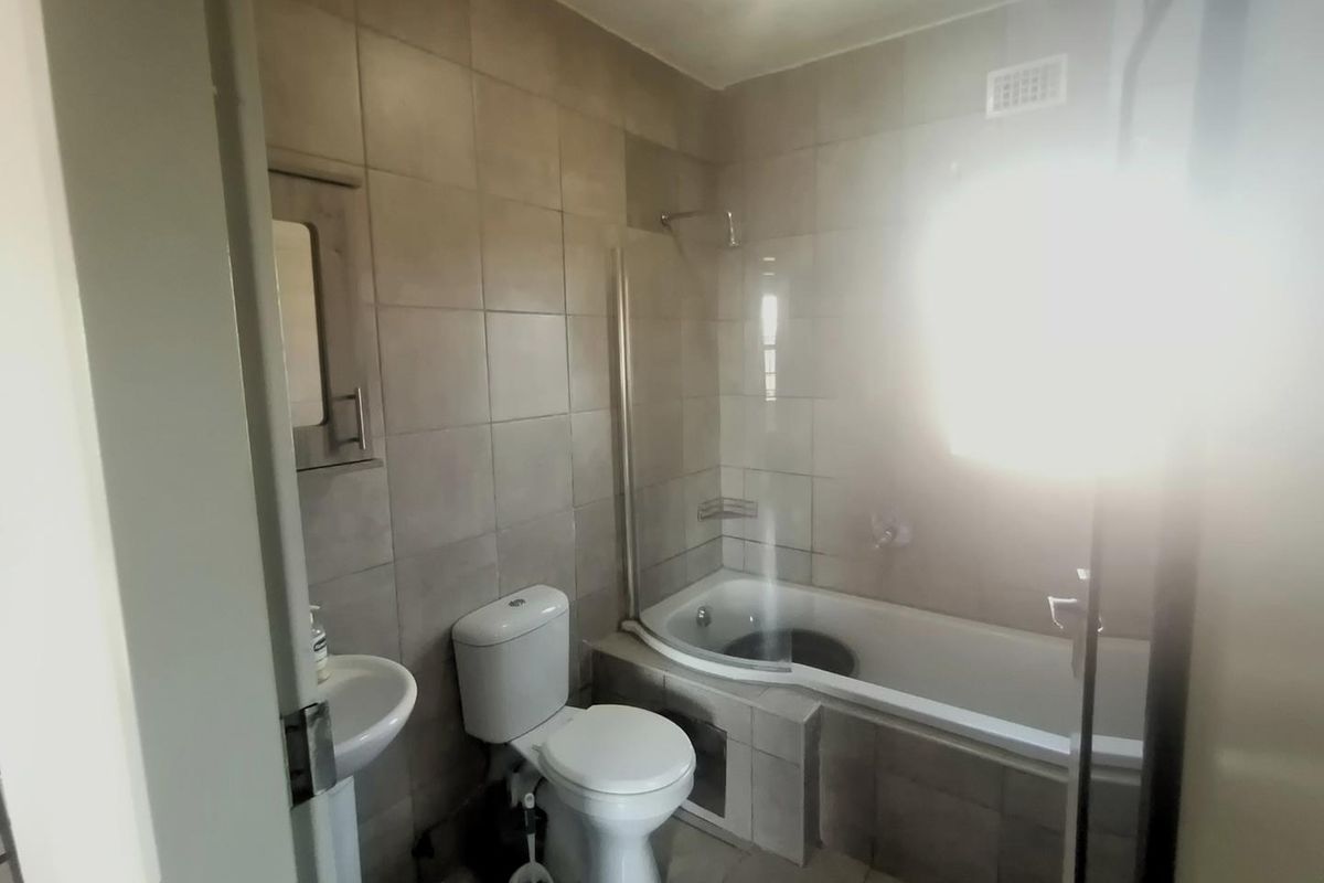 A functional bathroom featuring a bathtub with a glass shower screen, pedestal basin, and toilet, finished with neutral wall and floor tiling.