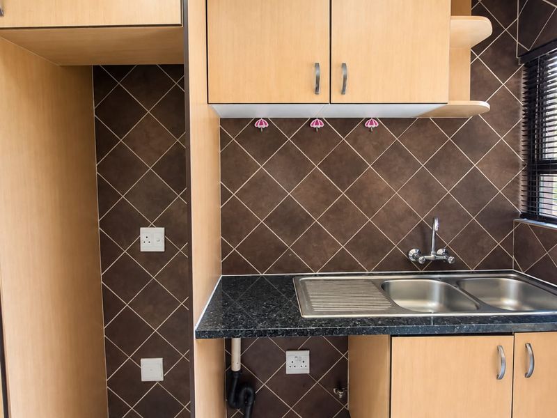 A functional kitchen area featuring light wood-tone cabinetry, a double stainless steel sink, and dark tiled splashbacks with ample space for appliances.