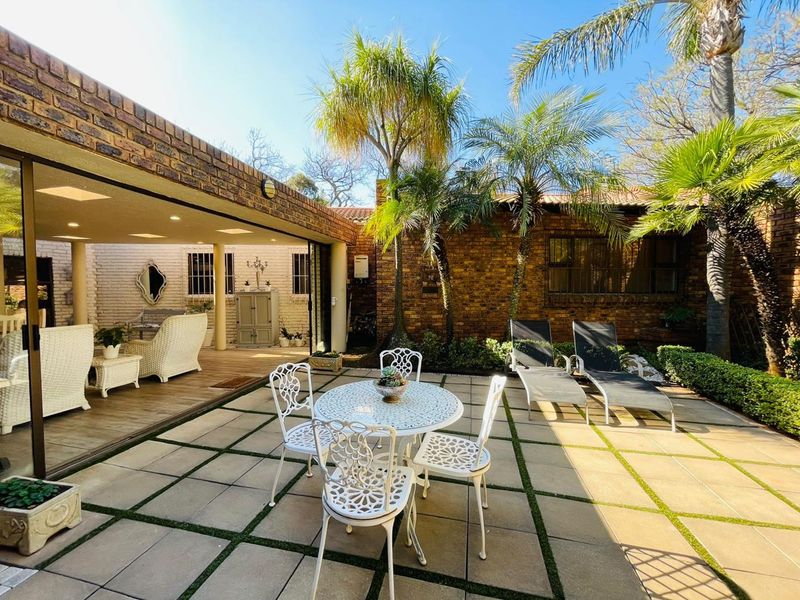 A spacious covered patio area with seamless indoor-outdoor flow, featuring brick construction, recessed lighting, and direct access to a landscaped garden terrace.