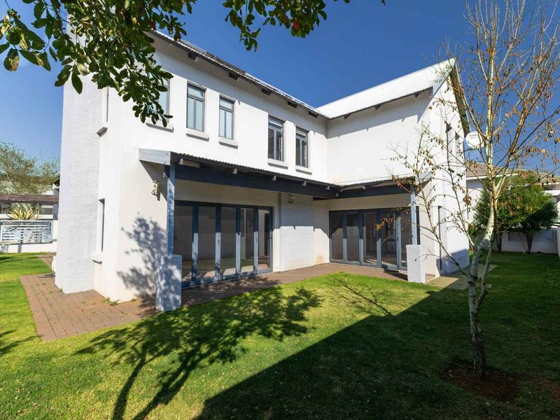Rear view of the house featuring a covered patio with folding glass doors, overlooking a well-maintained garden and lawn area.