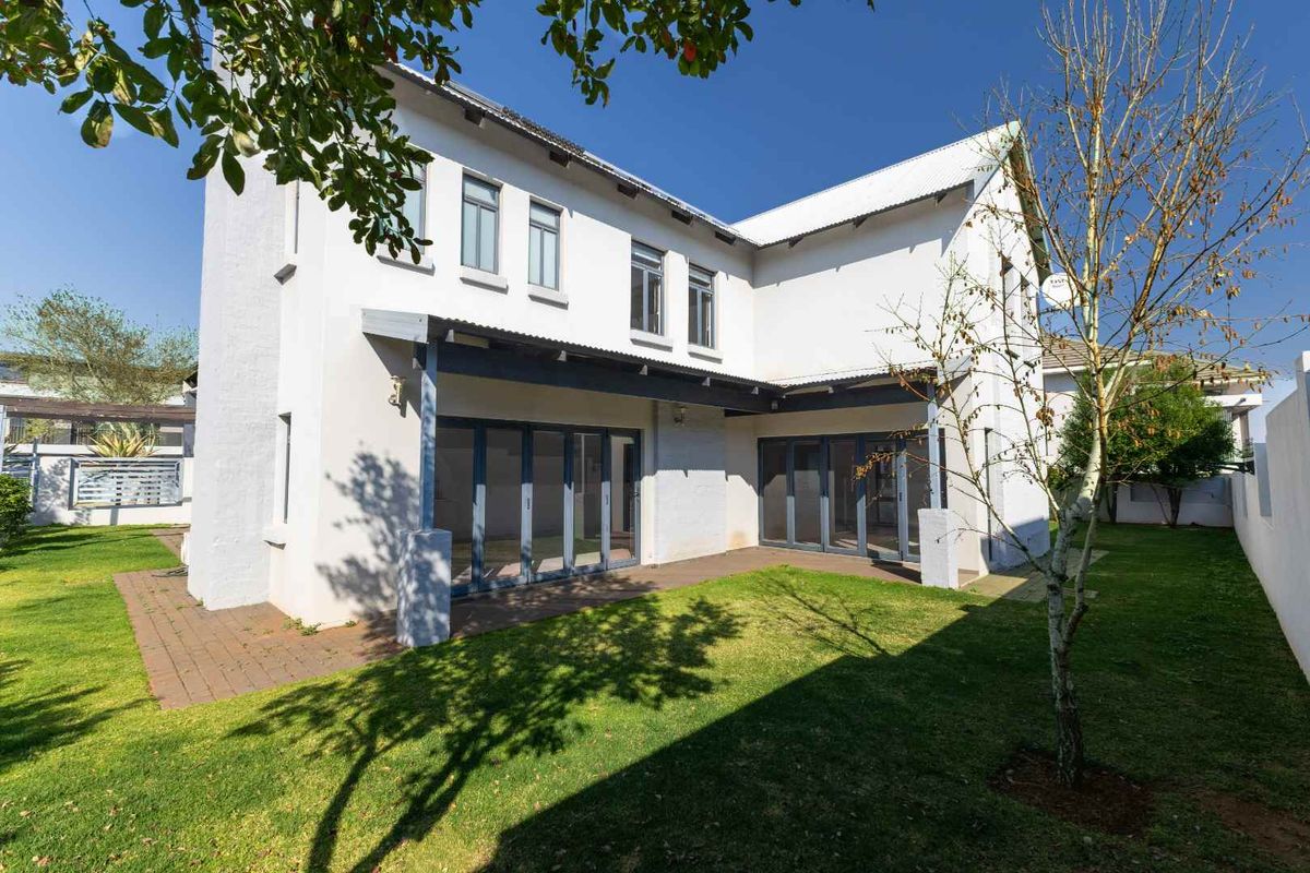 Rear view of the house featuring a covered patio with folding glass doors, overlooking a well-maintained garden and lawn area.