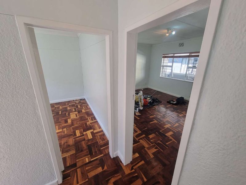 A view from the hallway looking into two empty bedrooms featuring classic parquet flooring and large windows.