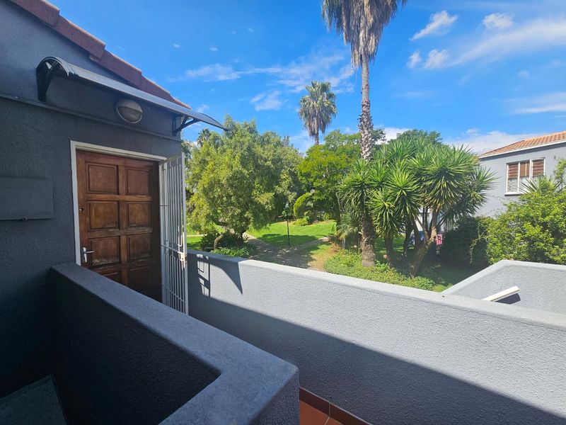 A private balcony area featuring a security gate, exterior lighting, and views over the communal garden space.