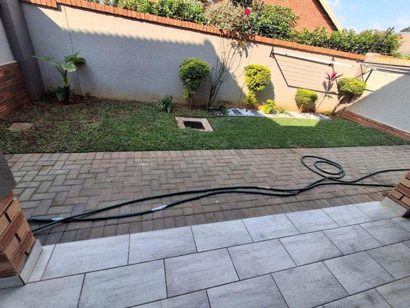 A private rear garden featuring a tiled patio area, paved walkway, and a well-maintained lawn enclosed by brick boundary walls.
