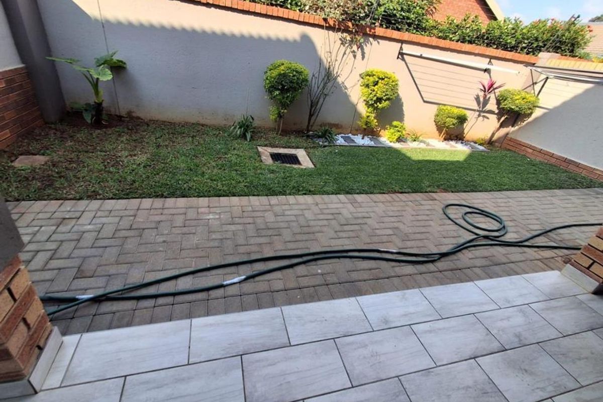 A private rear garden featuring a tiled patio area, paved walkway, and a well-maintained lawn enclosed by brick boundary walls.