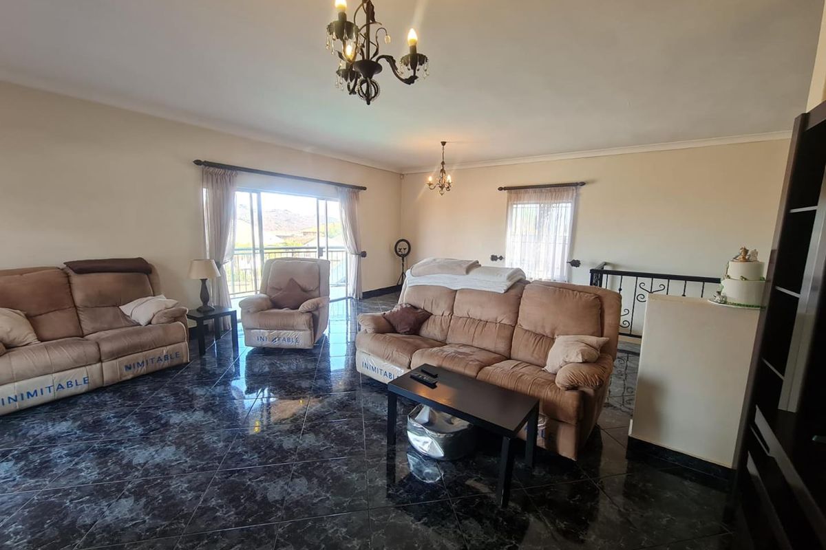 Spacious living area featuring dark marble-effect floor tiles, decorative chandeliers, and large sliding doors leading to an outdoor balcony.