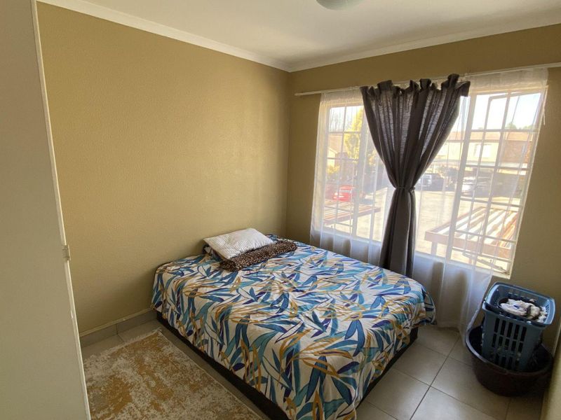 A standard bedroom featuring tiled flooring and a window fitted with security bars, providing natural light and a view of the exterior.