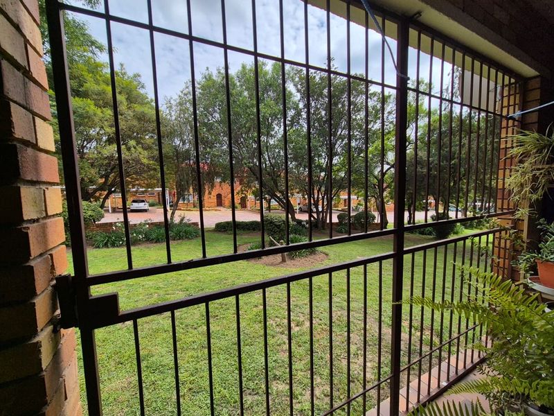 A covered patio area featuring a secure metal gate, overlooking a communal garden and parking area.