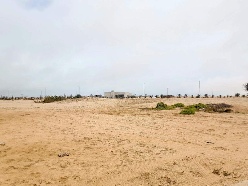 A wide-angle view of a vacant residential plot featuring sandy terrain and sparse natural vegetation in a developing area.