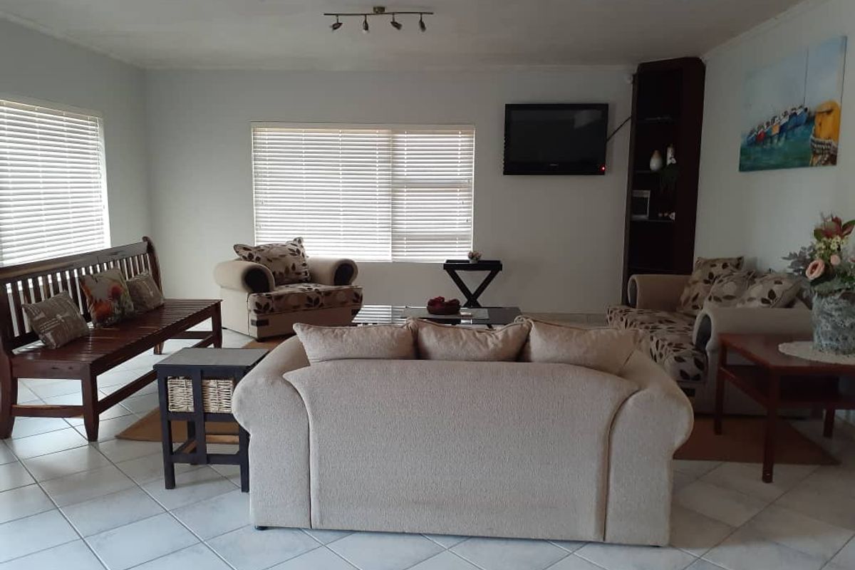 Spacious living room featuring tiled flooring, large windows with fitted blinds, and a built-in corner shelving unit.