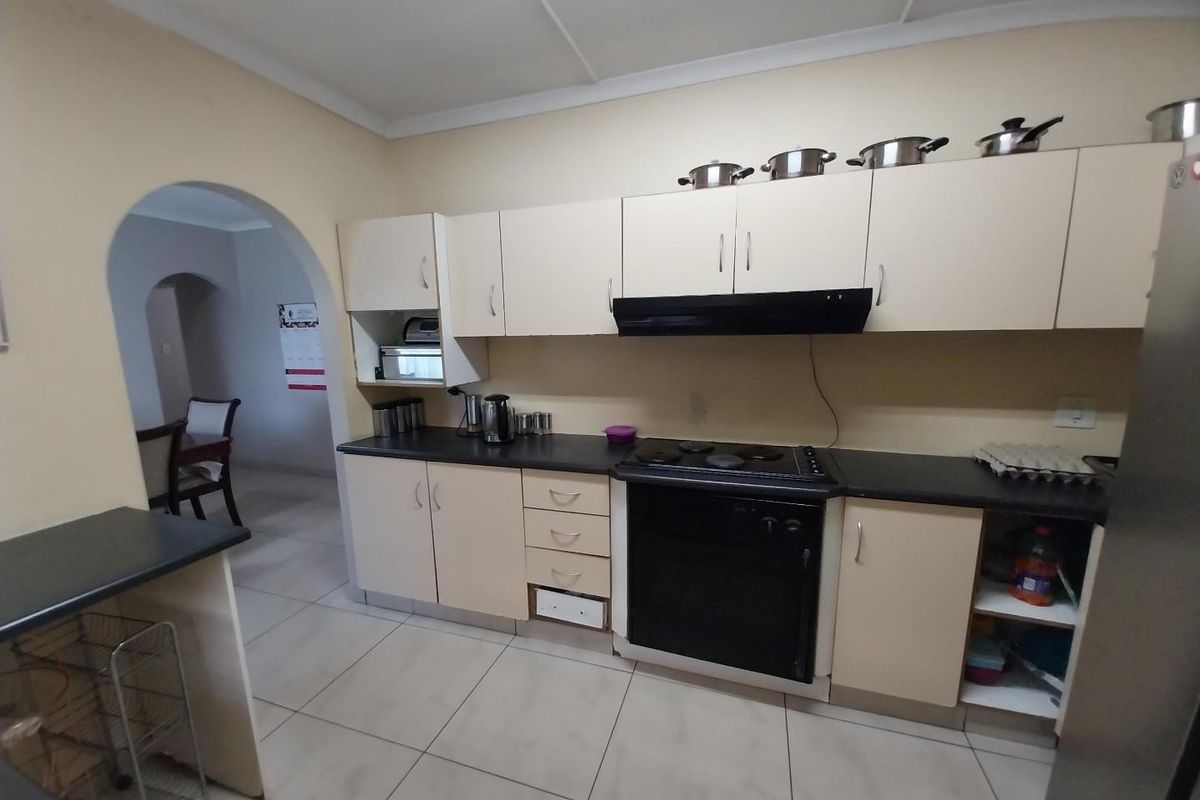A functional kitchen featuring built-in cabinetry, laminate countertops, and an integrated electric stove and oven, with tiled flooring and an arched entryway.