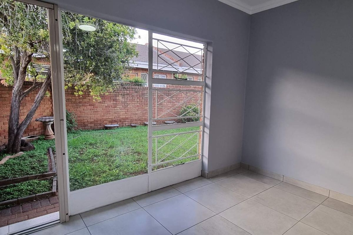 A bright, empty living area featuring large glass sliding doors with security gates, opening directly onto a private rear garden with brick boundary walls.