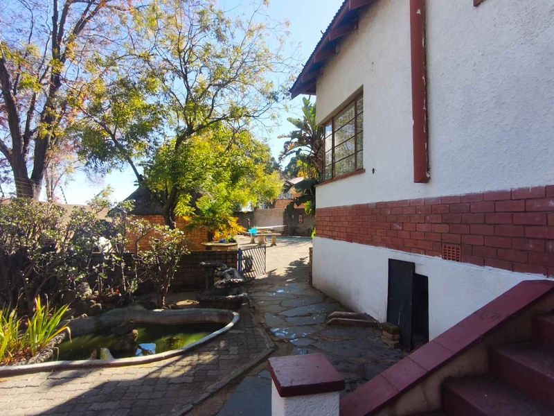 Rear exterior view of the property featuring a stone pathway, brick and plaster facade, and an ornamental garden pond.