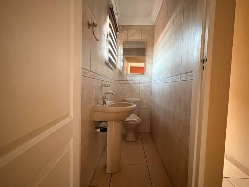 A compact, functional bathroom featuring tiled walls and flooring, a pedestal sink, and a toilet, offering a clean and practical layout.
