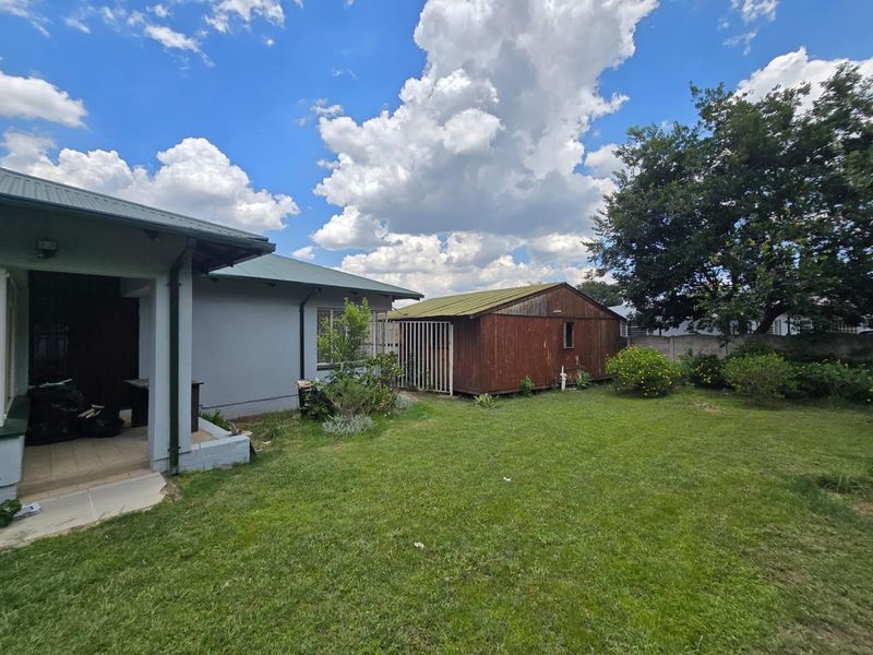 Rear view of the property featuring a lawn, covered patio area, and a detached wooden storage shed in the garden.