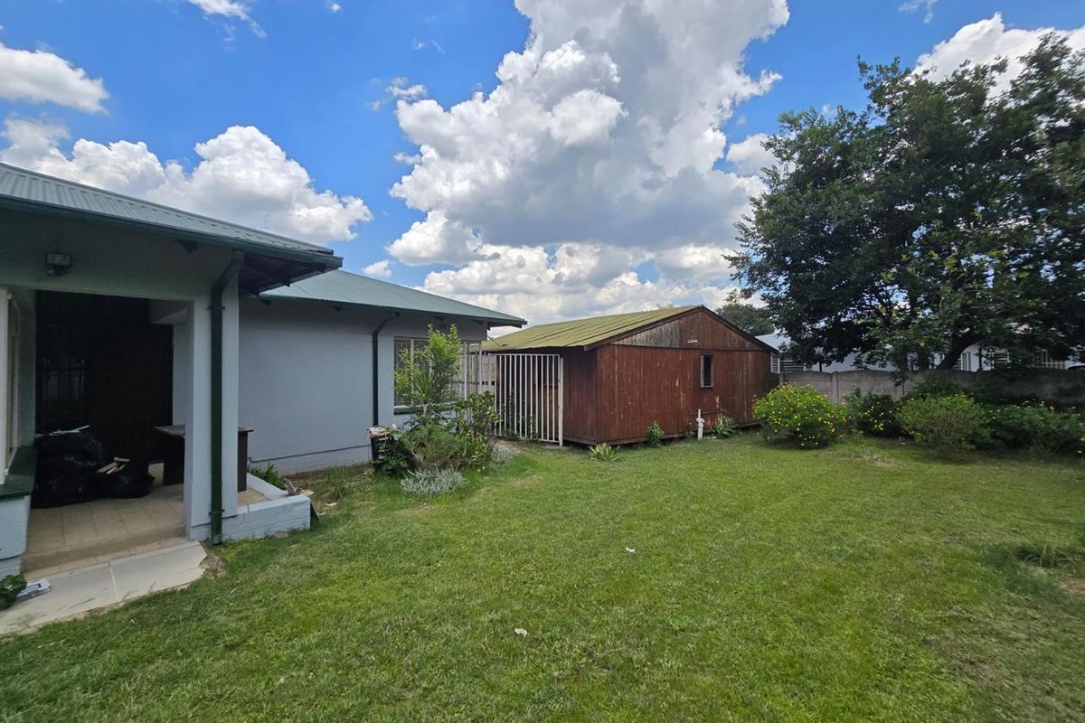 Rear view of the property featuring a lawn, covered patio area, and a detached wooden storage shed in the garden.