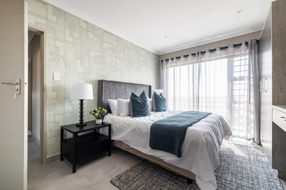 A well-lit bedroom featuring a textured feature wall, tiled flooring, and a large window with access to an outdoor area.