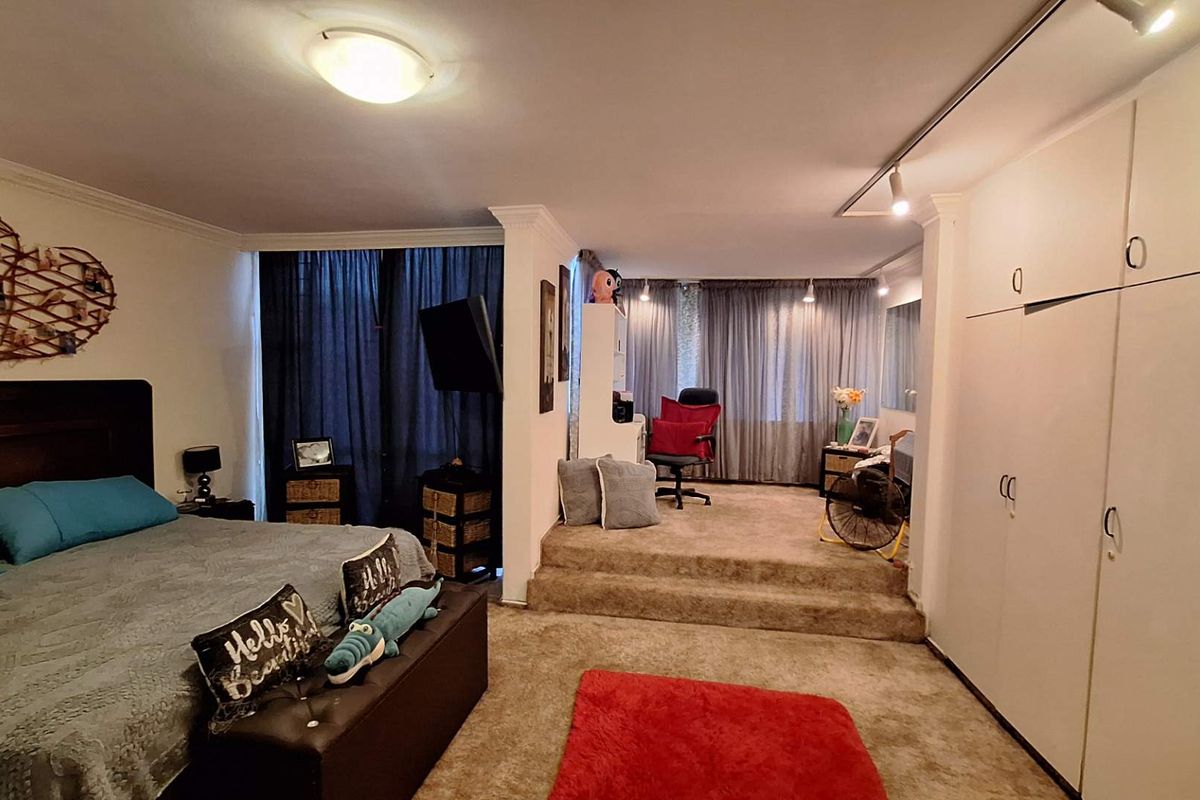 Spacious bedroom featuring a raised study or seating area, built-in wardrobes, and carpeted flooring throughout.