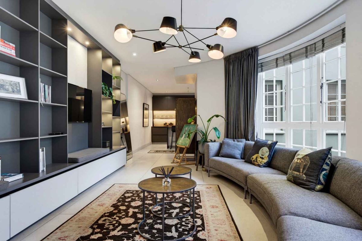 Modern living room featuring a large built-in shelving unit, tiled floors, and ample natural light from a multi-pane window.