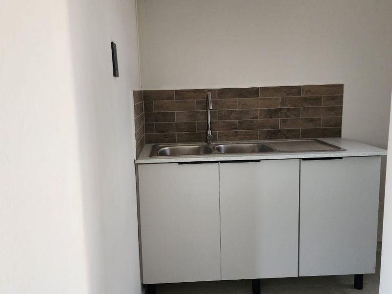 A compact scullery area featuring a double sink, modern base cabinetry, and a decorative tiled backsplash.